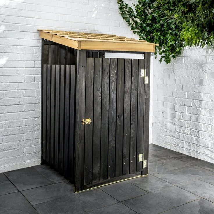 a black trash can sitting in front of a white brick wall with a wooden roof