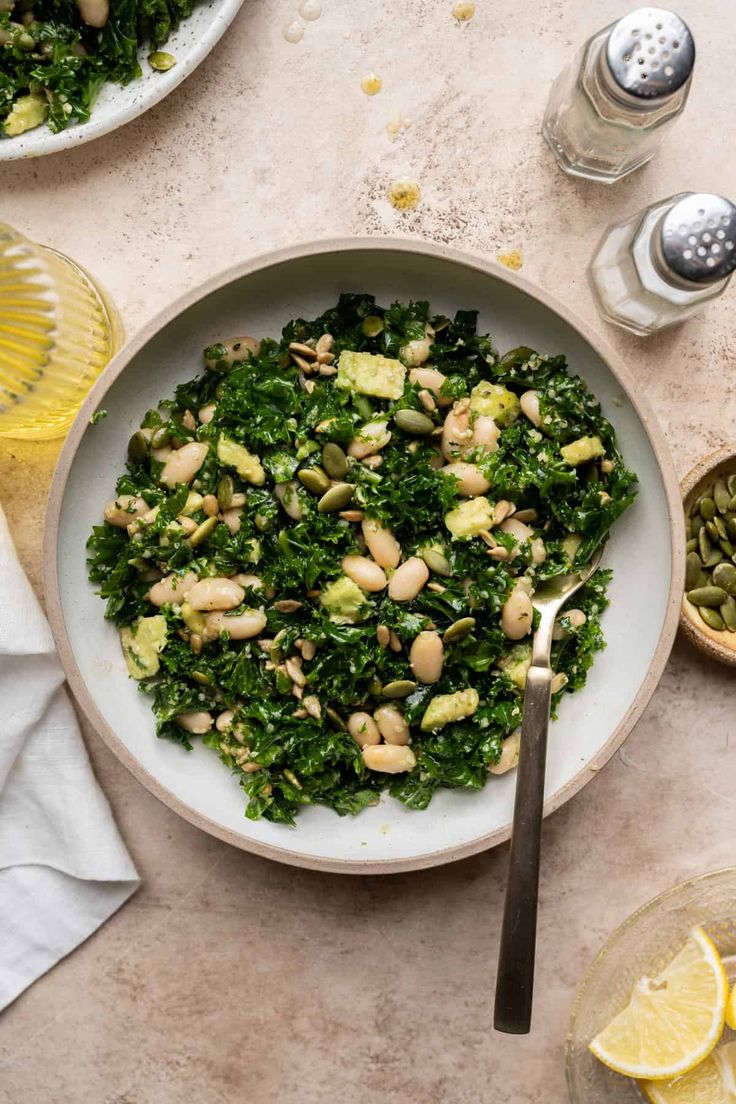 a white bowl filled with greens and nuts next to lemons on a counter top