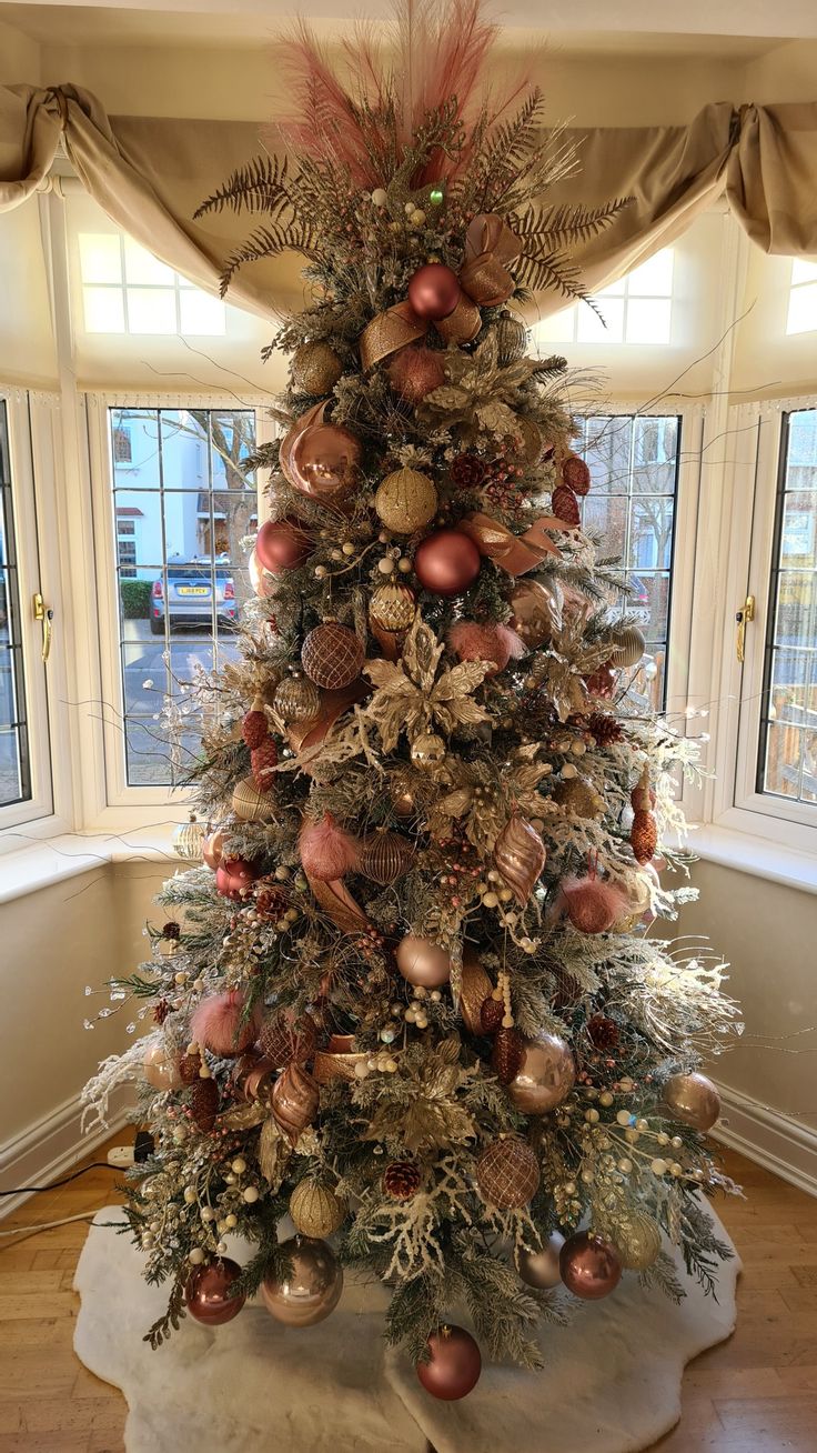 a decorated christmas tree in a living room with large windows and gold ornaments on the top