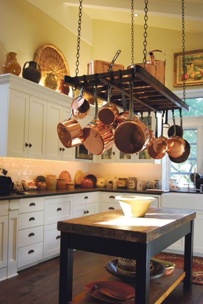 a kitchen filled with lots of pots and pans hanging from the ceiling over an island