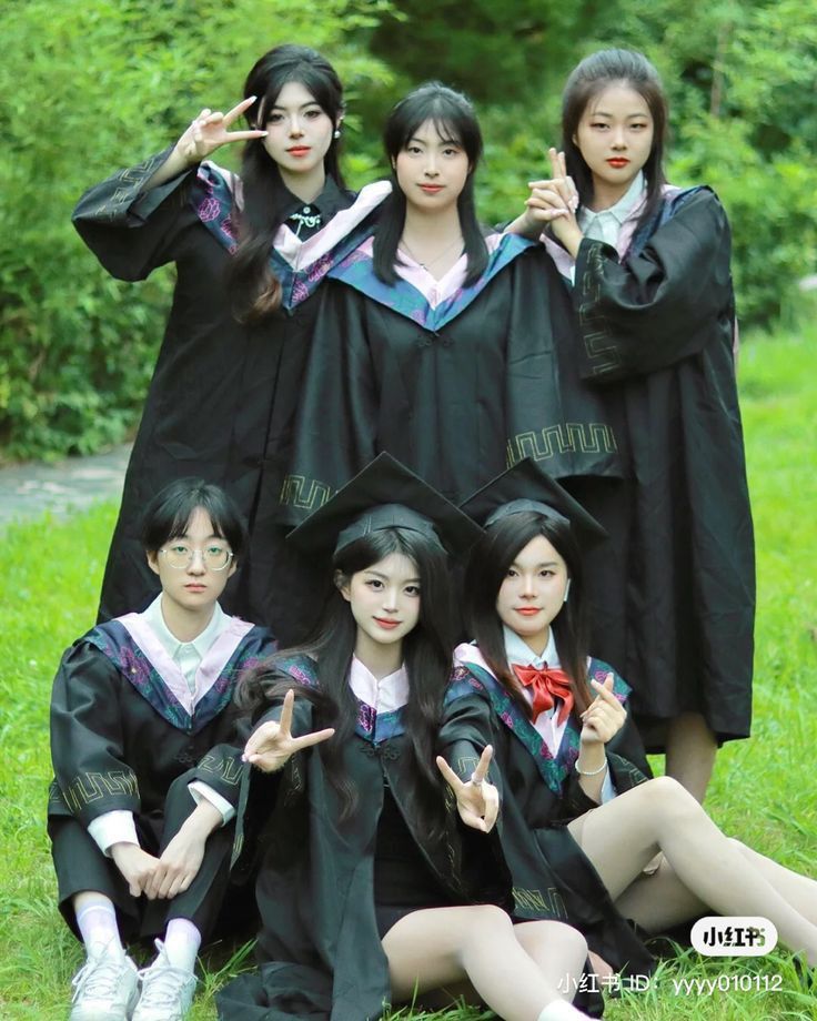 four young women dressed in graduation gowns posing for the camera with their fingers up