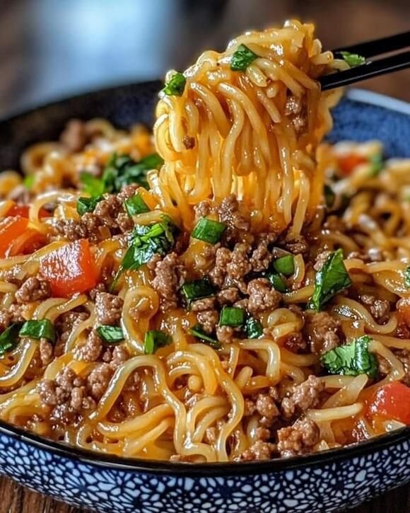 a close up of a bowl of noodles with meat and veggies being held by chopsticks