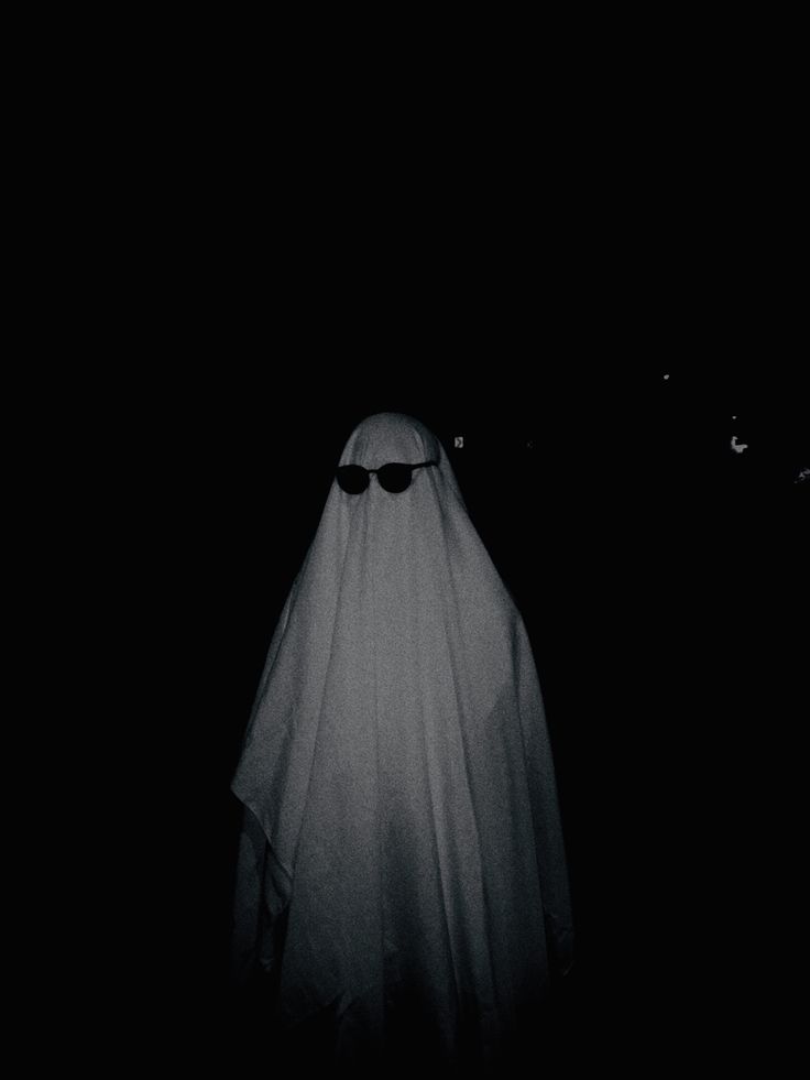 a person in a white ghost costume with sunglasses and a head scarf is standing in the dark