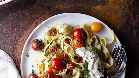 a white plate topped with pasta covered in sauce and cherry tomatoes next to a fork