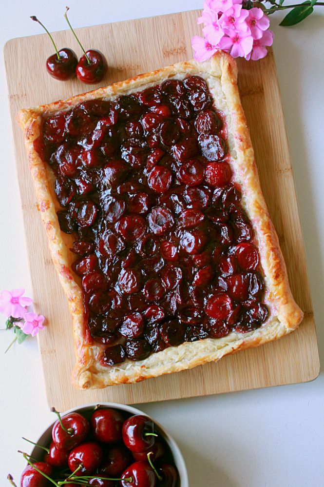 a cherry pie on a cutting board next to a bowl of cherries and flowers