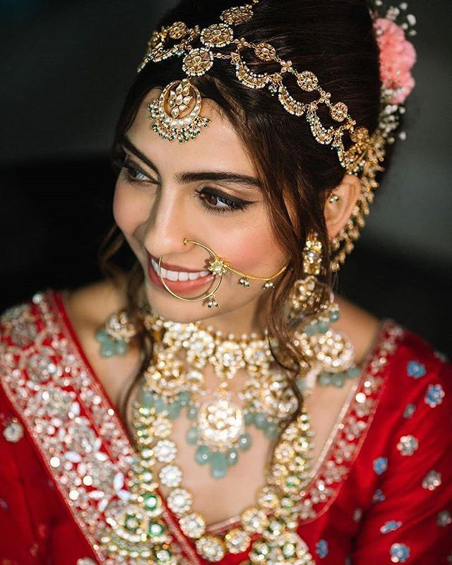 a woman wearing a red and gold bridal outfit with jewelry on her head, smiling at the camera