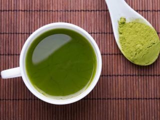 a cup of green tea next to a spoon