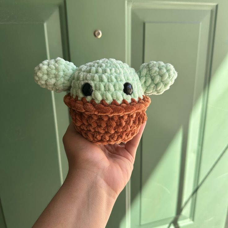 a hand holding a small crocheted toy in the shape of a yoda