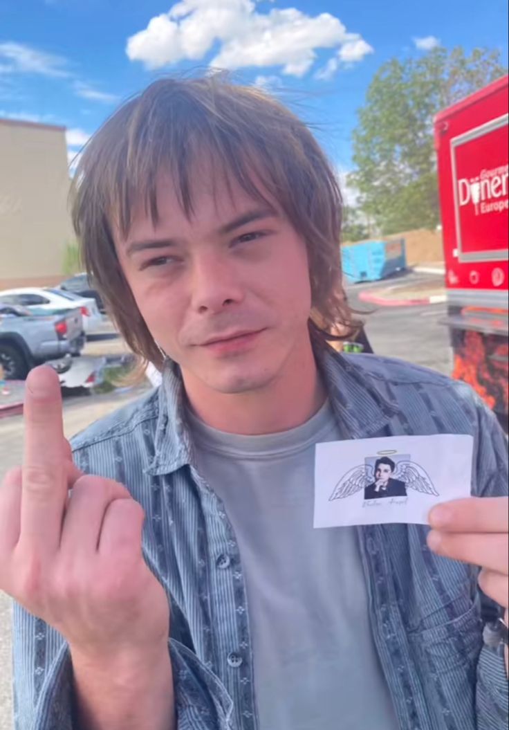 a young man is holding up his name tag and pointing to the camera with one hand