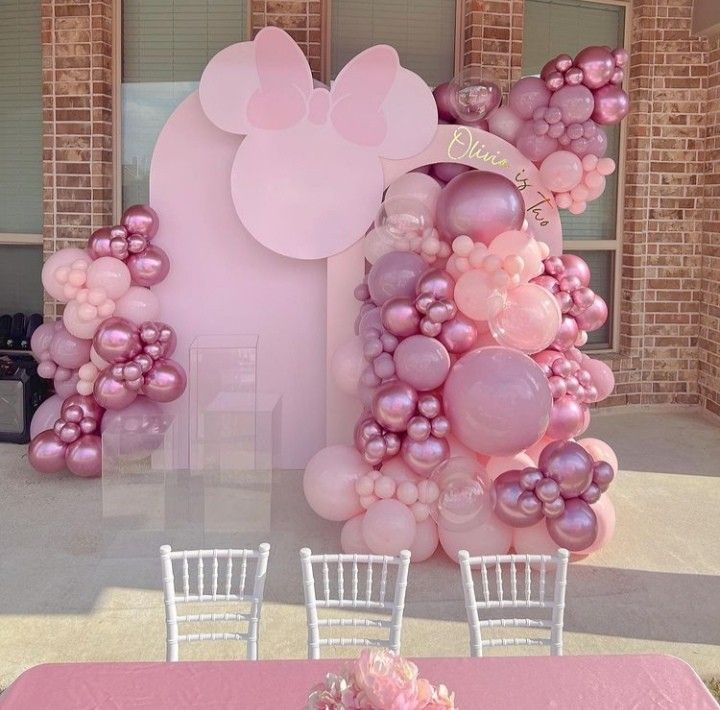 a table topped with lots of balloons next to a minnie mouse balloon wall and chair