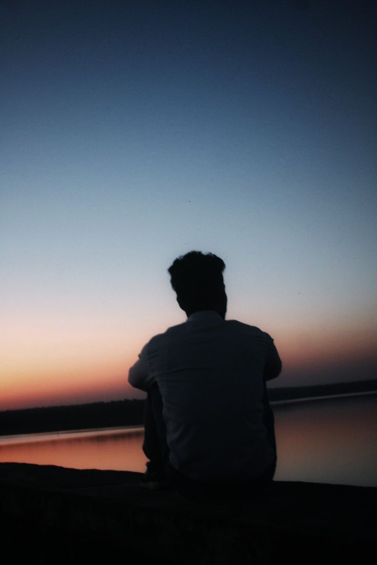 a man sitting on the edge of a pier watching the sunset