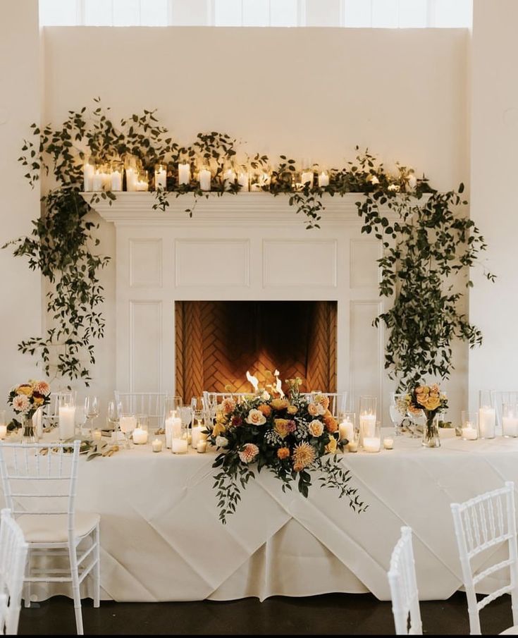 a table with candles, flowers and greenery is set up in front of a fireplace