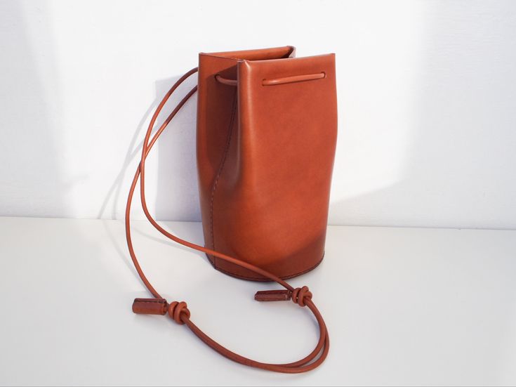 "Classic yet contemporary bucket bag, combined a minimalism and functional. The body made from Italian vegetan leather, using leather cord for the shoulder strap. The shoulder strap is adjustable, able to enjoy this bag for 3 ways as a crossbody bag, one-shoulder bag and handbag. Has a card sized inside pocket. Approximate Dimensions: W 4.75\" x H 8\" x D 4.75\" W 12cm x H 20cm x D 12cm Inside pocket W 3.50\" x H 3.50\" W 9.5cm x H 9.5cm - 100% Vegetable tanned leather (body) - Genuine leather c Modern Leather Shoulder Bag With Long Strap, Minimalist Bucket Shoulder Bag With Adjustable Strap, Minimalist Crossbody Bucket Bag For Travel, Minimalist Office Bucket Bag With Adjustable Strap, Minimalist Bucket Shoulder Bag With Leather Handles, Daily Use Crossbody Bucket Bag With Leather Strap, Daily Use Leather Strap Crossbody Bucket Bag, Minimalist Crossbody Bucket Bag For Office, Leather Strap Crossbody Bucket Bag For Daily Use