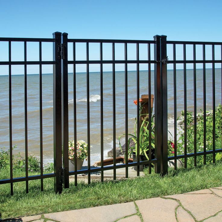 an iron fence overlooking the ocean on a sunny day with green grass and flowers in pots