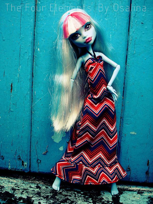 a doll with long blonde hair wearing a red and blue dress standing in front of a wooden door