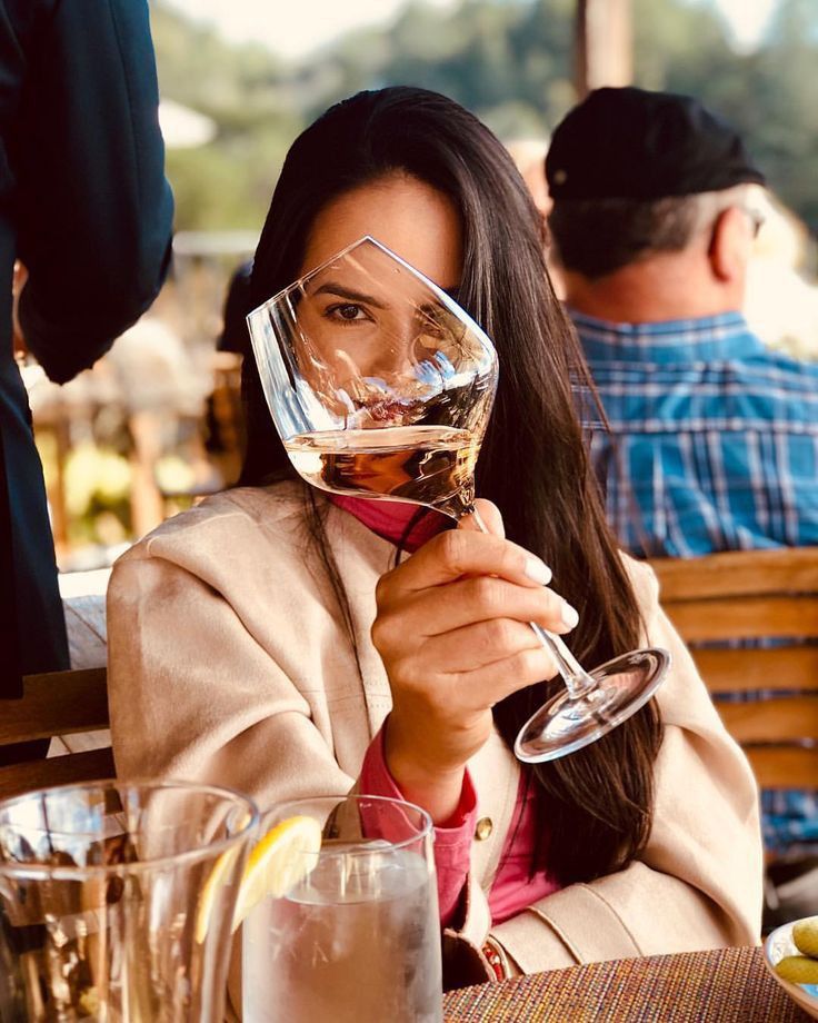 a woman sitting at a table with a glass of wine in front of her face