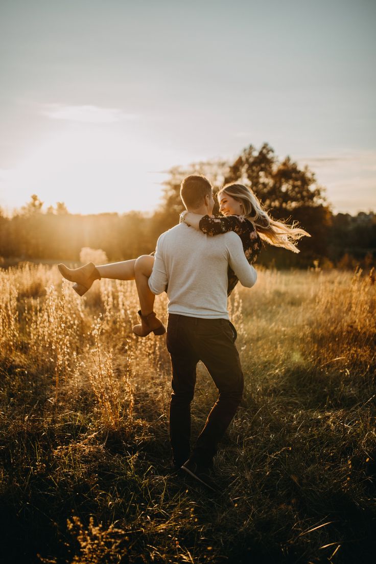 a man carrying a woman on his back in an open field at sunset with the sun behind him