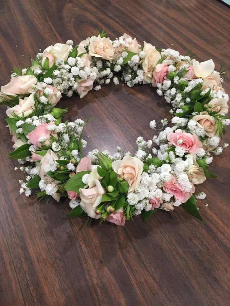 a flower wreath on a wooden table with white and pink flowers in the shape of a heart