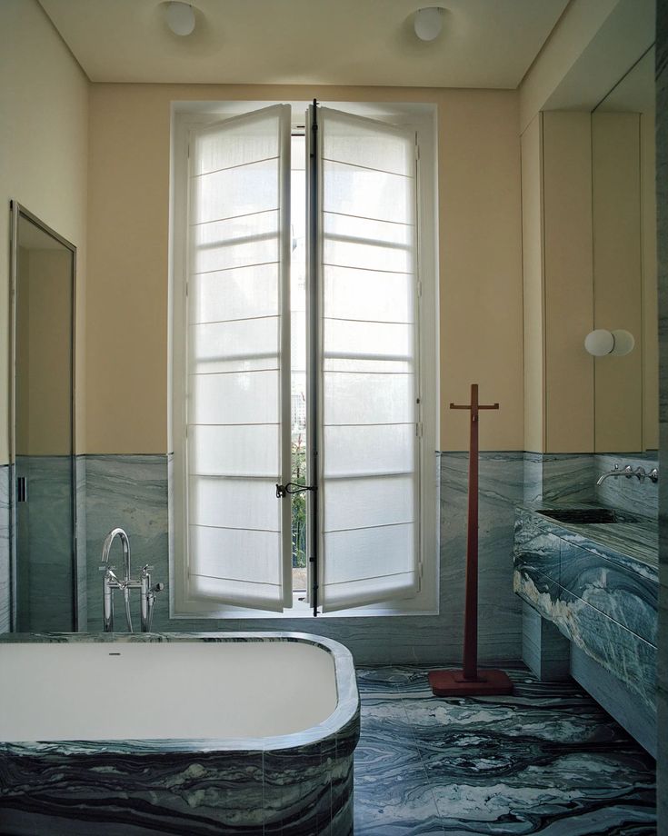 a bath tub sitting in the middle of a bathroom next to a tall white window