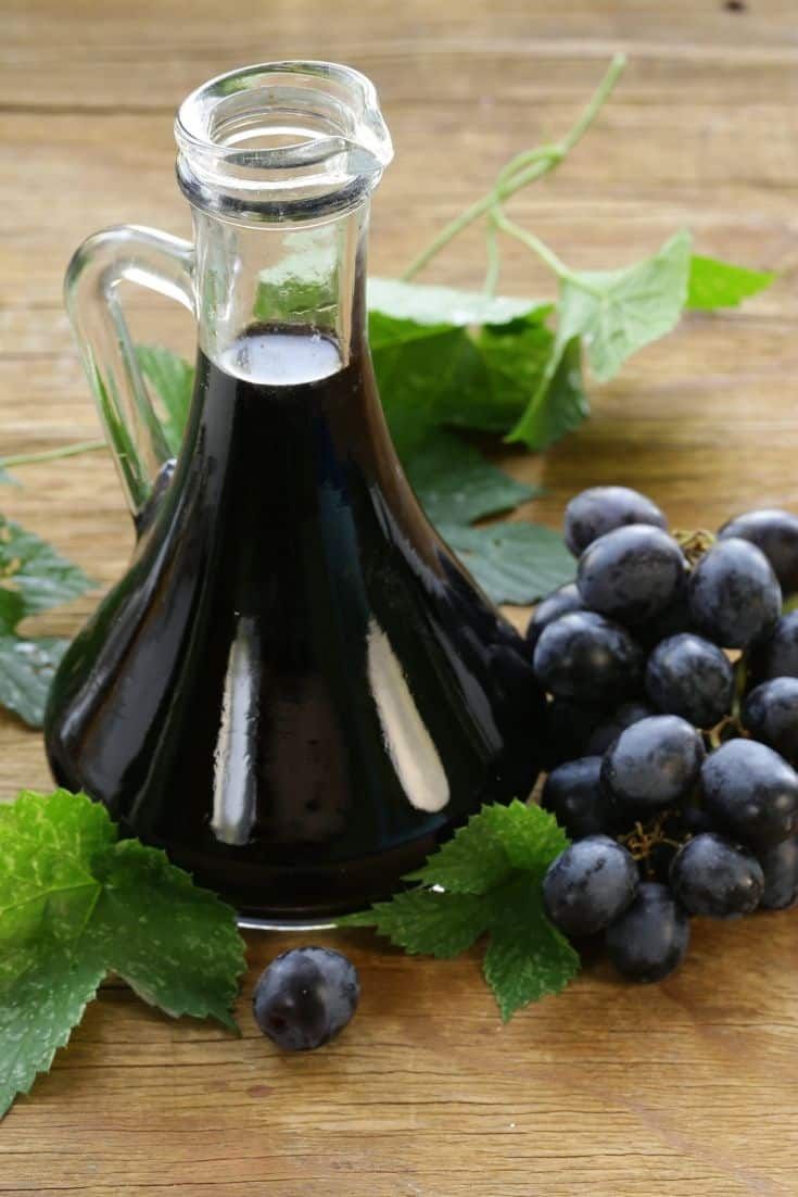 a bottle of black wine next to grapes and leaves on a wooden table with green leaves