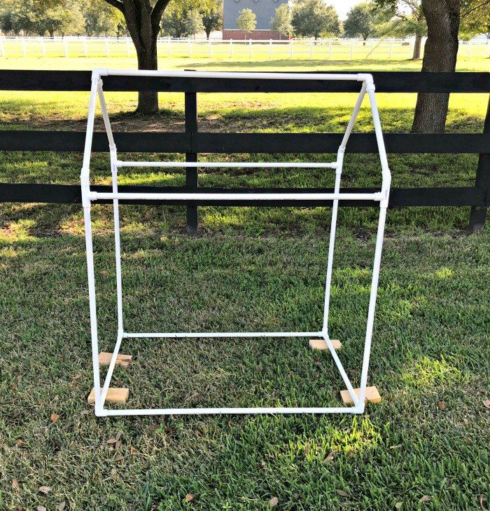 a white metal clothes rack sitting on top of grass next to a tree and fence