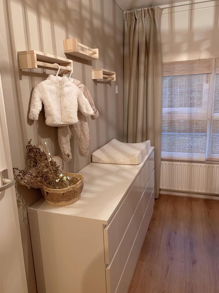 a baby's changing table in the corner of a room with clothes hanging on hooks