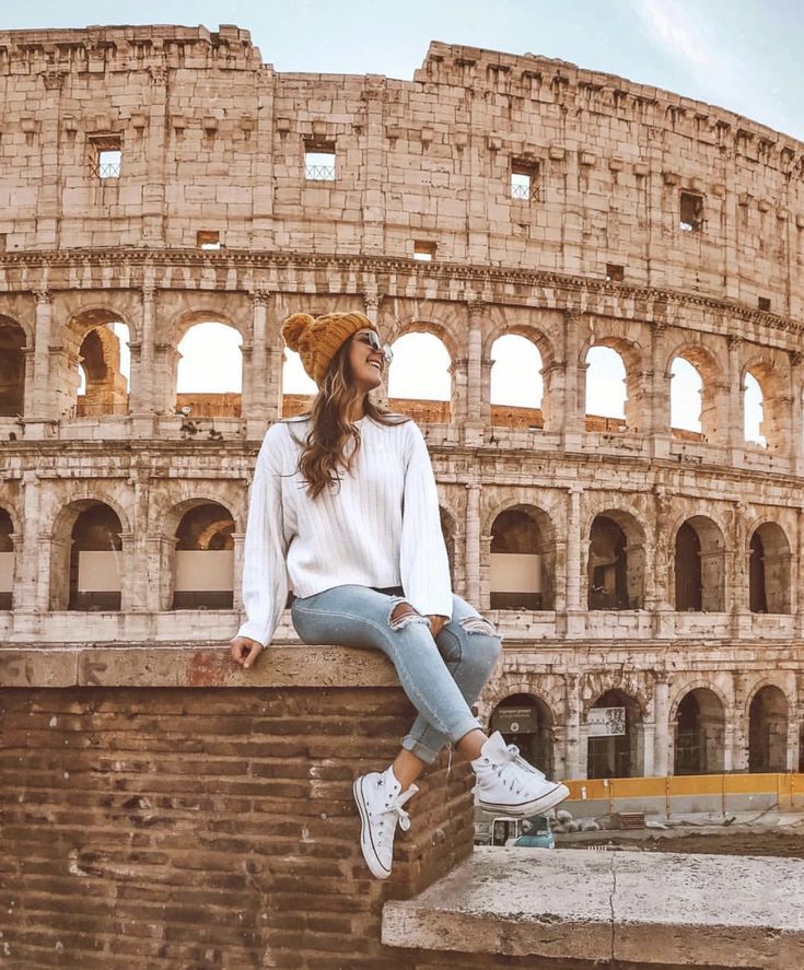 a woman sitting on top of a brick wall next to an old roman collise