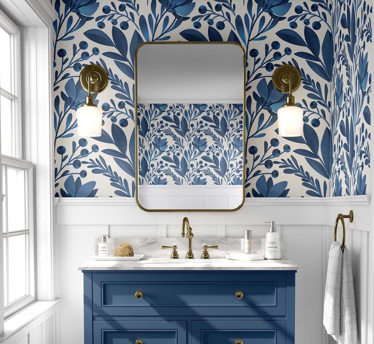 a bathroom with blue and white wallpaper, gold fixtures and a large mirror over the sink