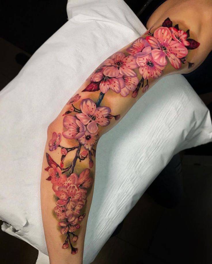 a woman's leg with flowers on it and the arm is covered in tattoos