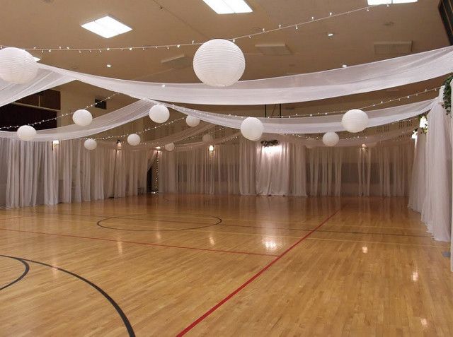 an indoor basketball court is decorated with white drapes and paper lanterns hanging from the ceiling