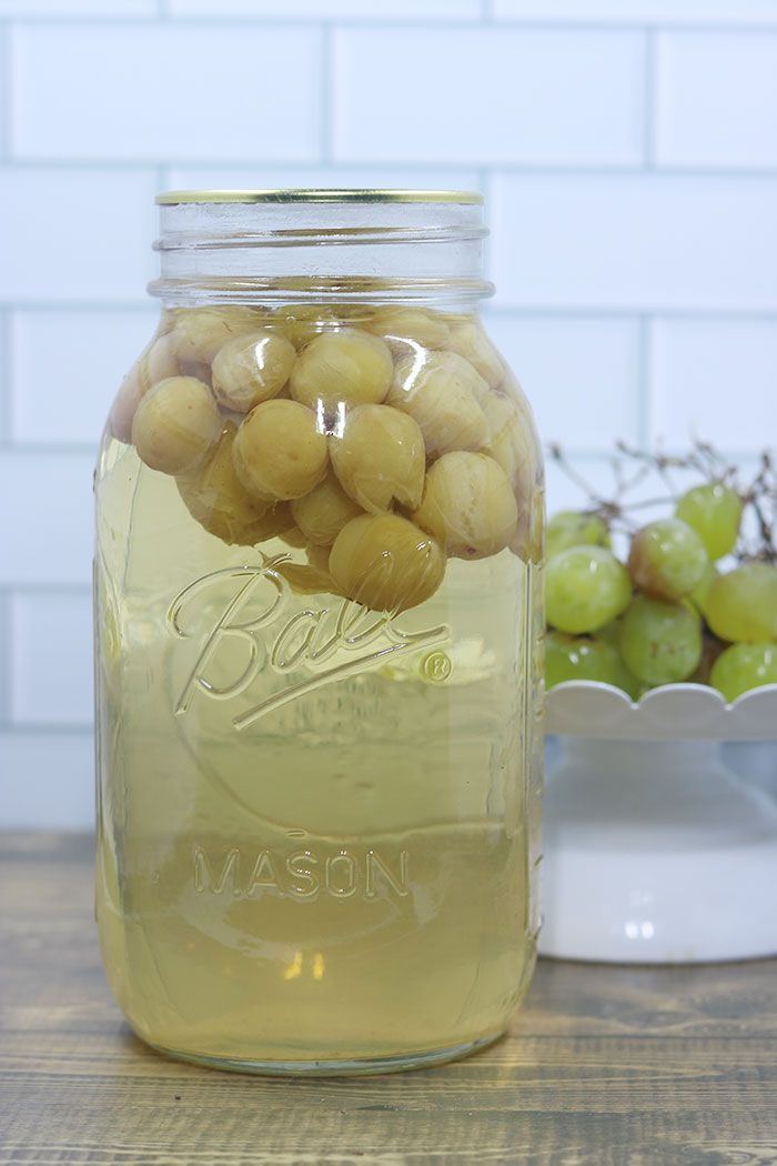 a jar filled with grapes sitting on top of a table next to a bowl of grapes