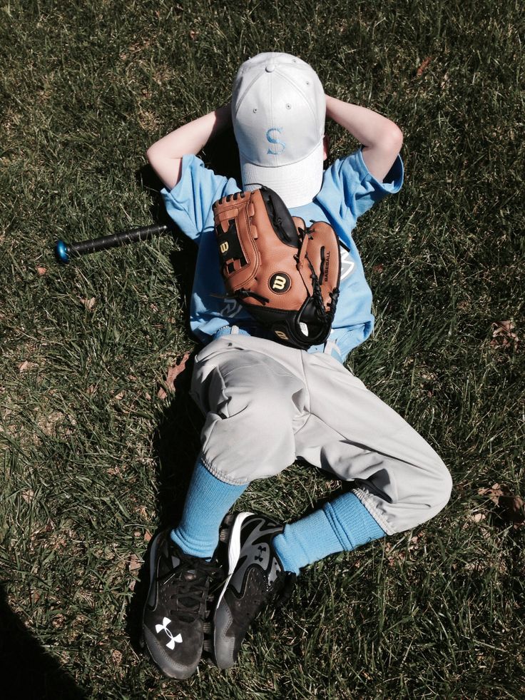 a young boy laying on the ground with a baseball glove and ball in his hand