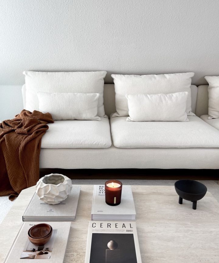 a white couch sitting next to a table with books on it and candles in front of it