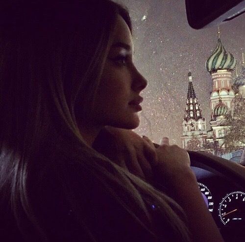 a woman sitting in the passenger seat of a car looking out at an urban skyline