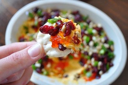 a hand holding up a scoop of food with fruit and nuts on it in a white bowl