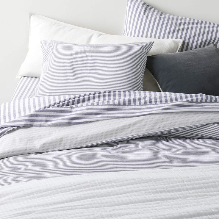 an unmade bed with blue and white striped sheets, pillows and pillowcases