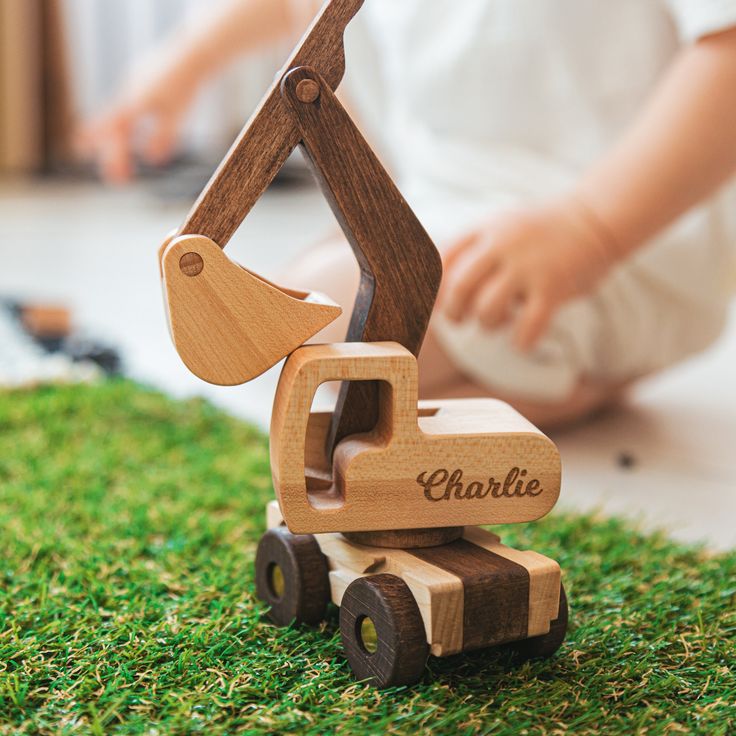 a wooden toy car with name on it sitting in the grass next to a child's hand