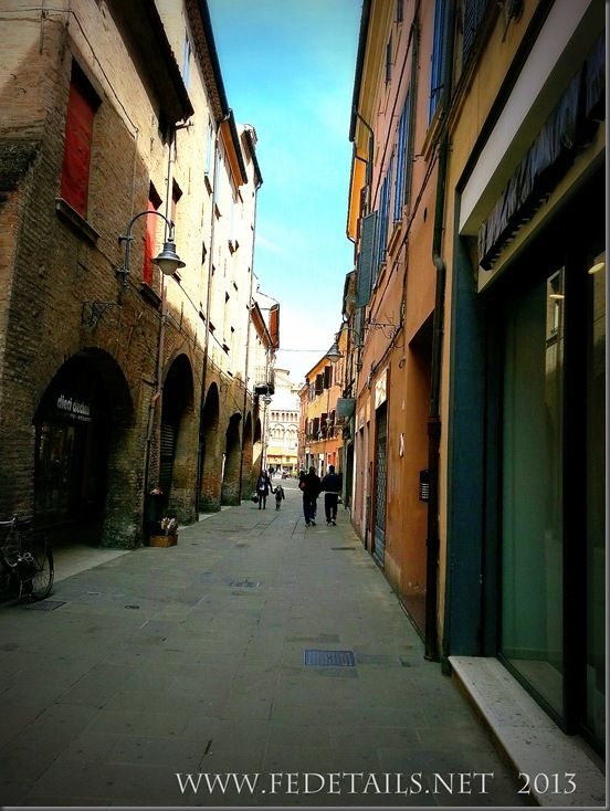 an alley way with people walking down it and buildings on both sides that have red shutters