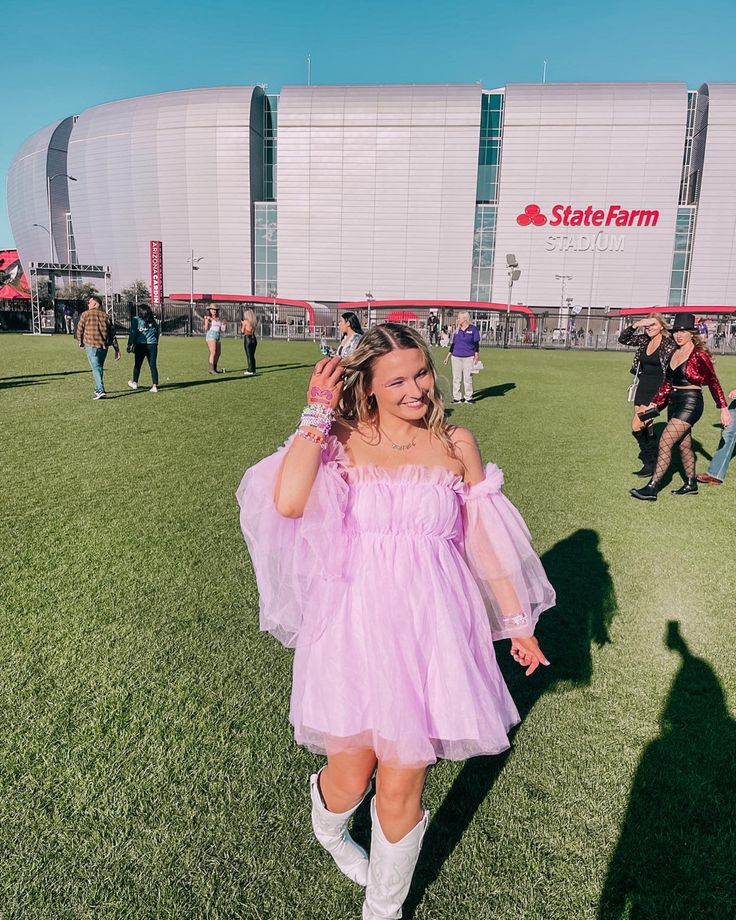 a girl in a pink dress is walking on the grass with her hands behind her head