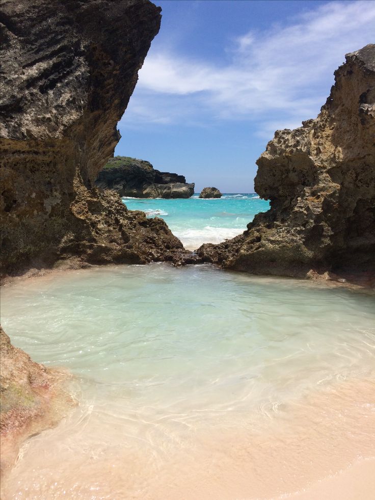 the water is crystal blue and clear in this beach scene, with rocks sticking out from the sand