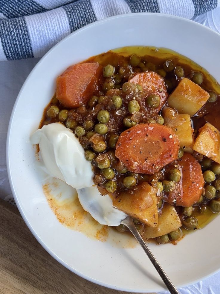 a white bowl filled with peas and carrots next to a spoon on top of a wooden table