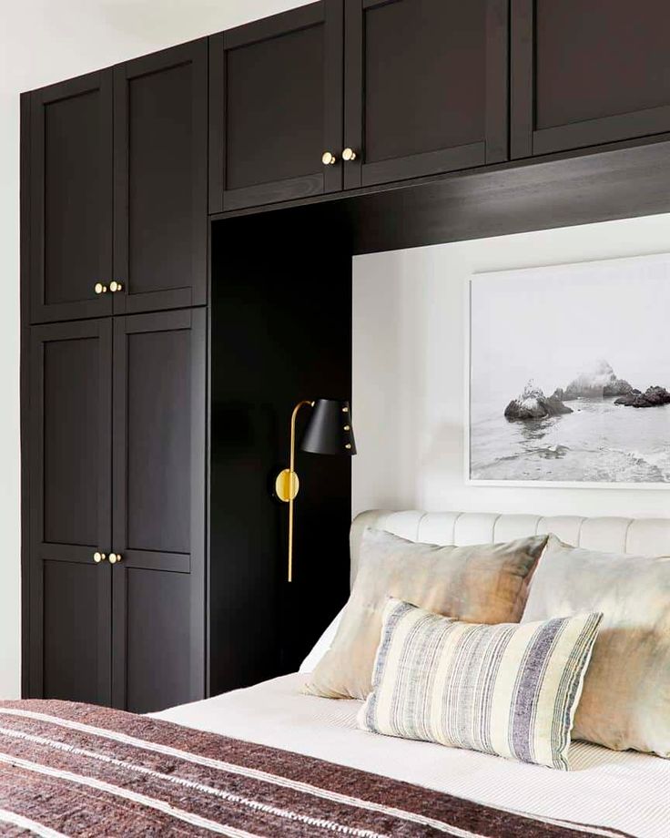 a bedroom with black cabinets, white bedding and a gold accent light on the wall