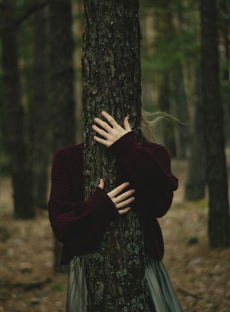 a woman is hugging a tree in the woods with her hands on it's face