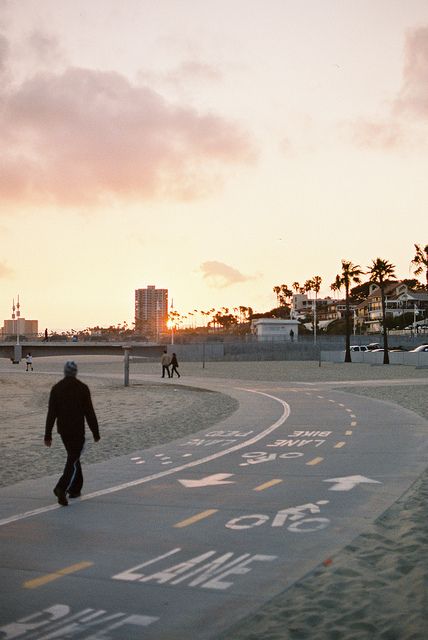 a man riding a skateboard down a sidewalk next to the ocean at sunset with palm trees