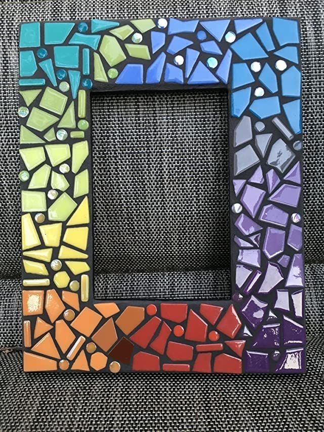 a multicolored mosaic frame sitting on top of a gray cloth covered chair with the letter e painted in it