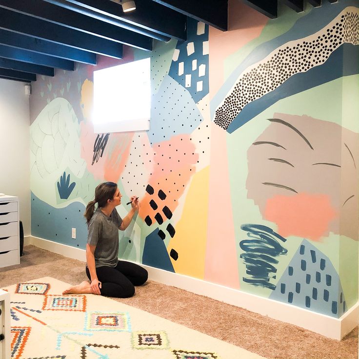 a woman sitting on the floor in front of a wall painting