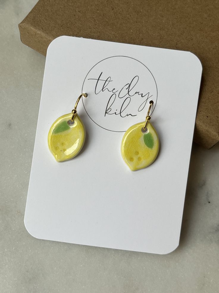 a pair of yellow and green earrings sitting on top of a white card next to a brown box