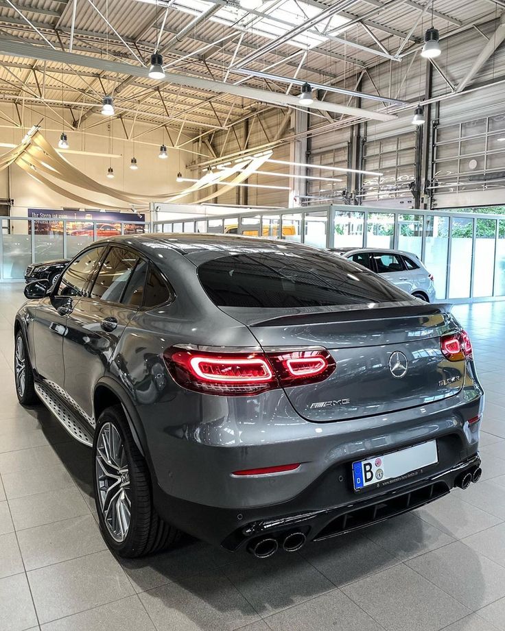 the rear end of a grey car in a showroom with two other cars behind it