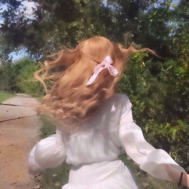 a woman with long red hair is walking down the street and has her hair blowing in the wind