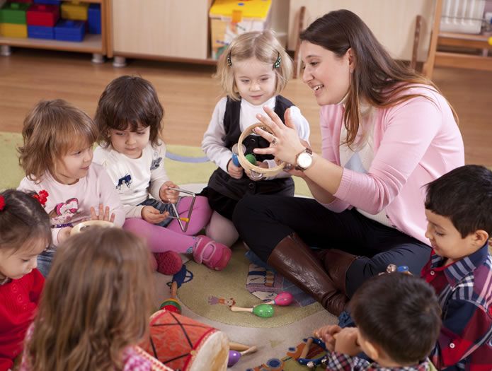 a woman sitting on the floor surrounded by children and playing with an object in front of her